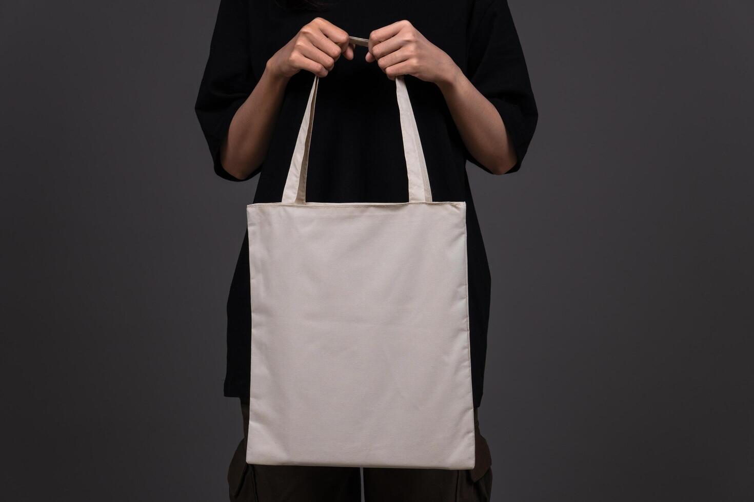 Front View of Woman Holding Blank Canvas Tote Bag, Eco-Friendly Reusable Fabric with Handle, Close-Up Mockup, No Plastic and Environmental Concept Dark Background photo