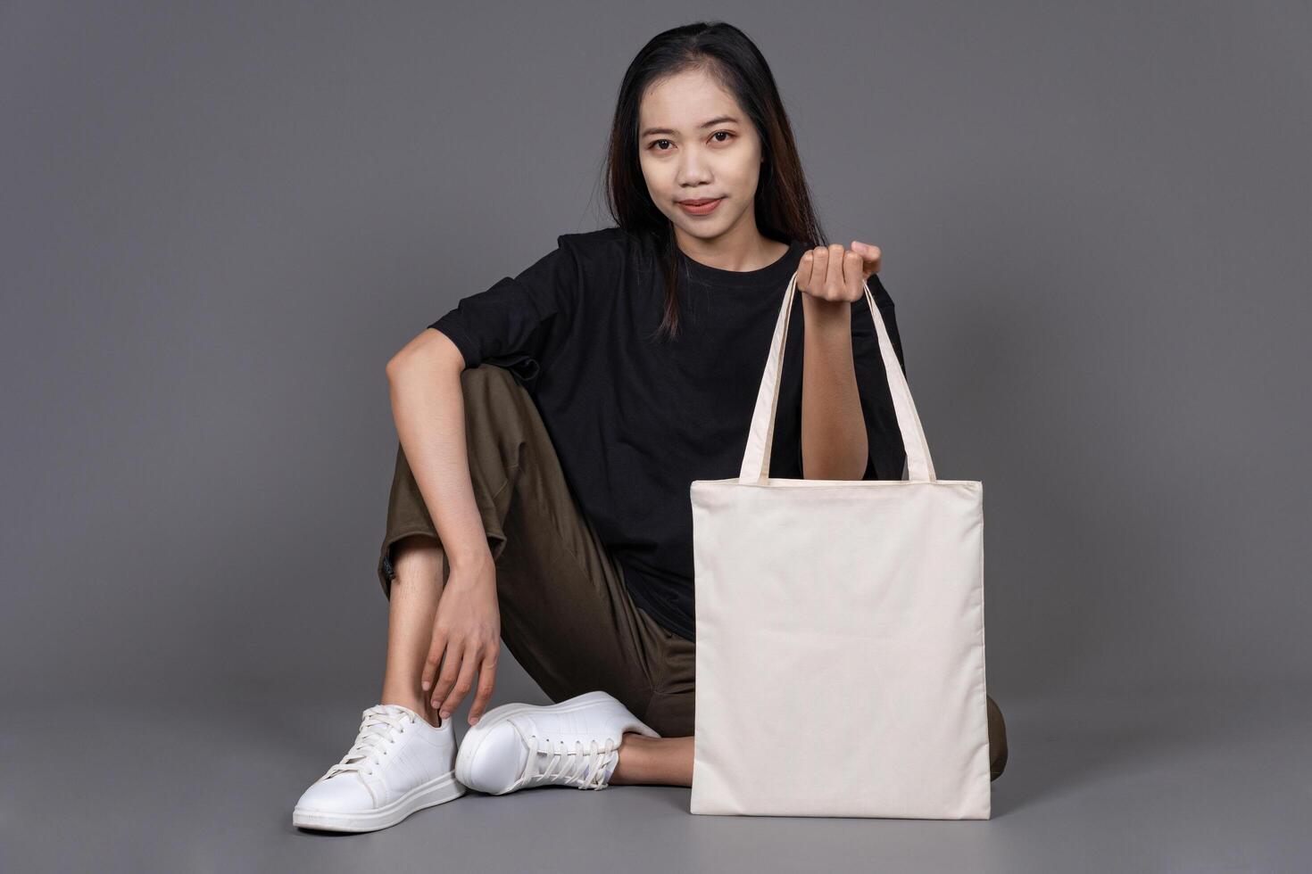 Female Sitting on Floor Holding Blank Canvas Tote Bag, Eco-Friendly Reusable Fabric with Handle, Close-Up Mockup, No Plastic and Environmental Concept photo