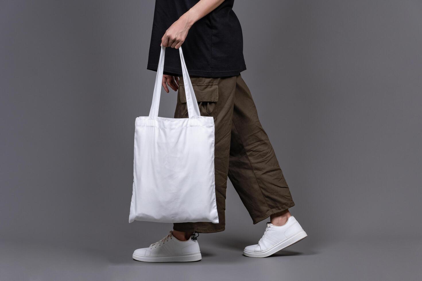 Woman Walking While Holding Blank Canvas Tote Bag, Eco-Friendly Reusable Fabric with Handle, Close-Up Mockup, No Plastic and Environmental Concept Isolated photo