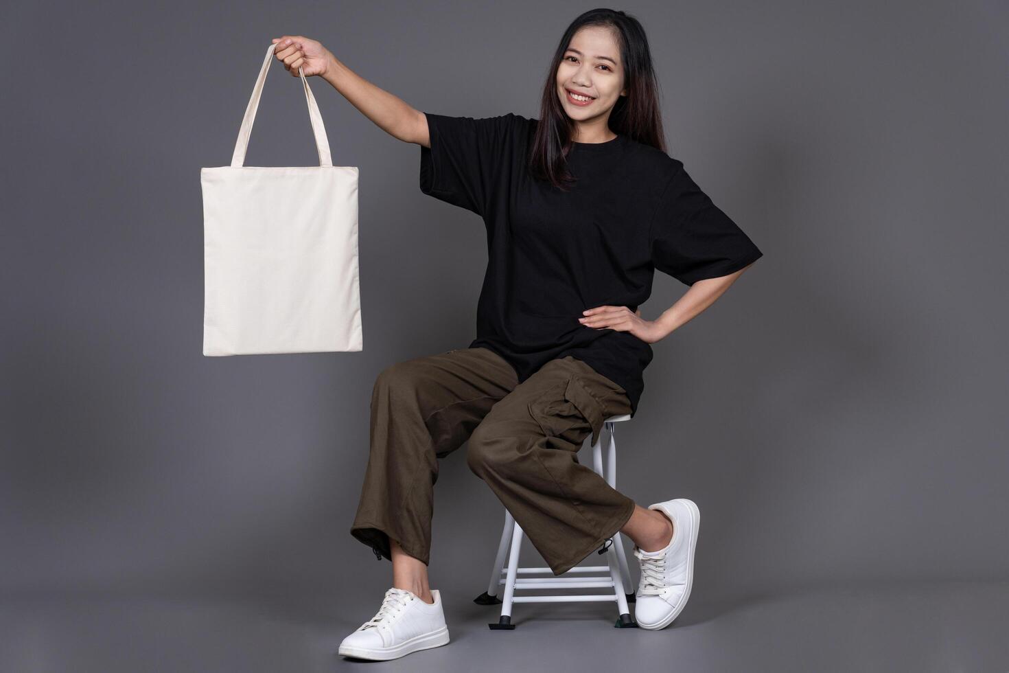 Female Sitting on Chair Holding Blank Canvas Tote Bag, Eco-Friendly Reusable Fabric with Handle, Close-Up Mockup, No Plastic and Environmental Concept photo