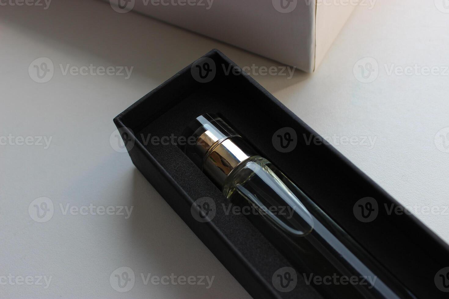 Black gift box with perfume near a white cardboard case on a white surface photo