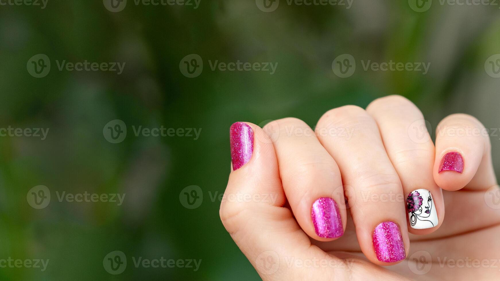 Female hand with pink manicure. Woman fingernails with pink holographic nail polish lacquer on green lush background. Aesthetic visual of red violet manicure with lady silhouette stamping. Copy space photo