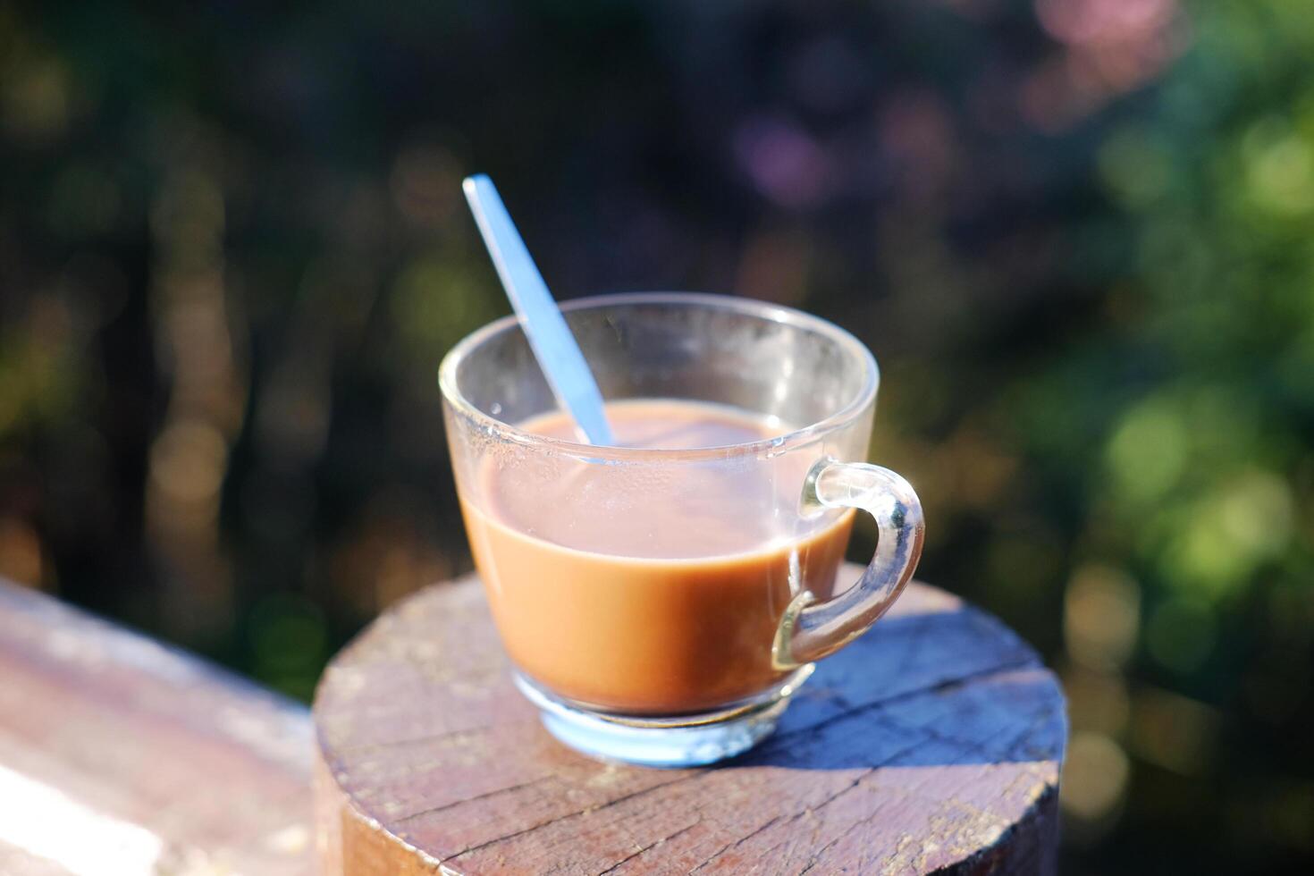 Close up a glass cup of hot coffee on wooden fence with the valley mountain in natural sunlight of morning and bright day In Thailand photo