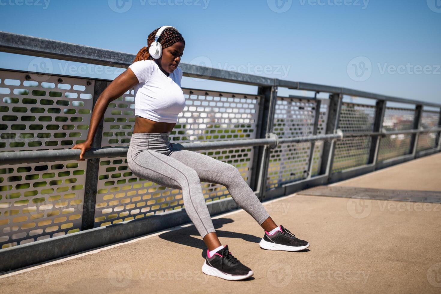 Young African-American woman doing reverse push-ups outdoors on a city bridge, showing strength and focus during her workout routine. photo