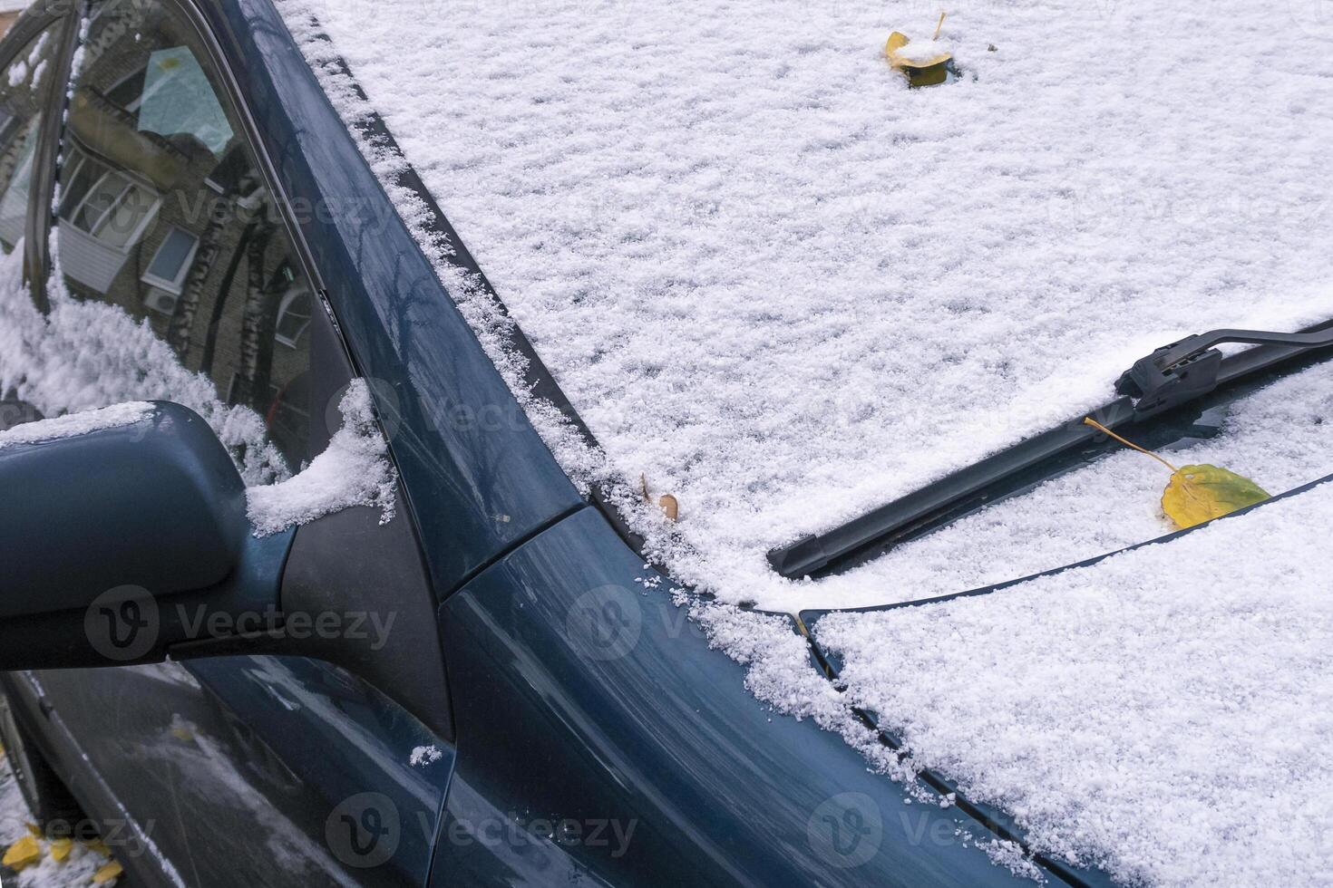 Blue car covered with snow and a few autumn leaves. Late autumn or winter scene. photo