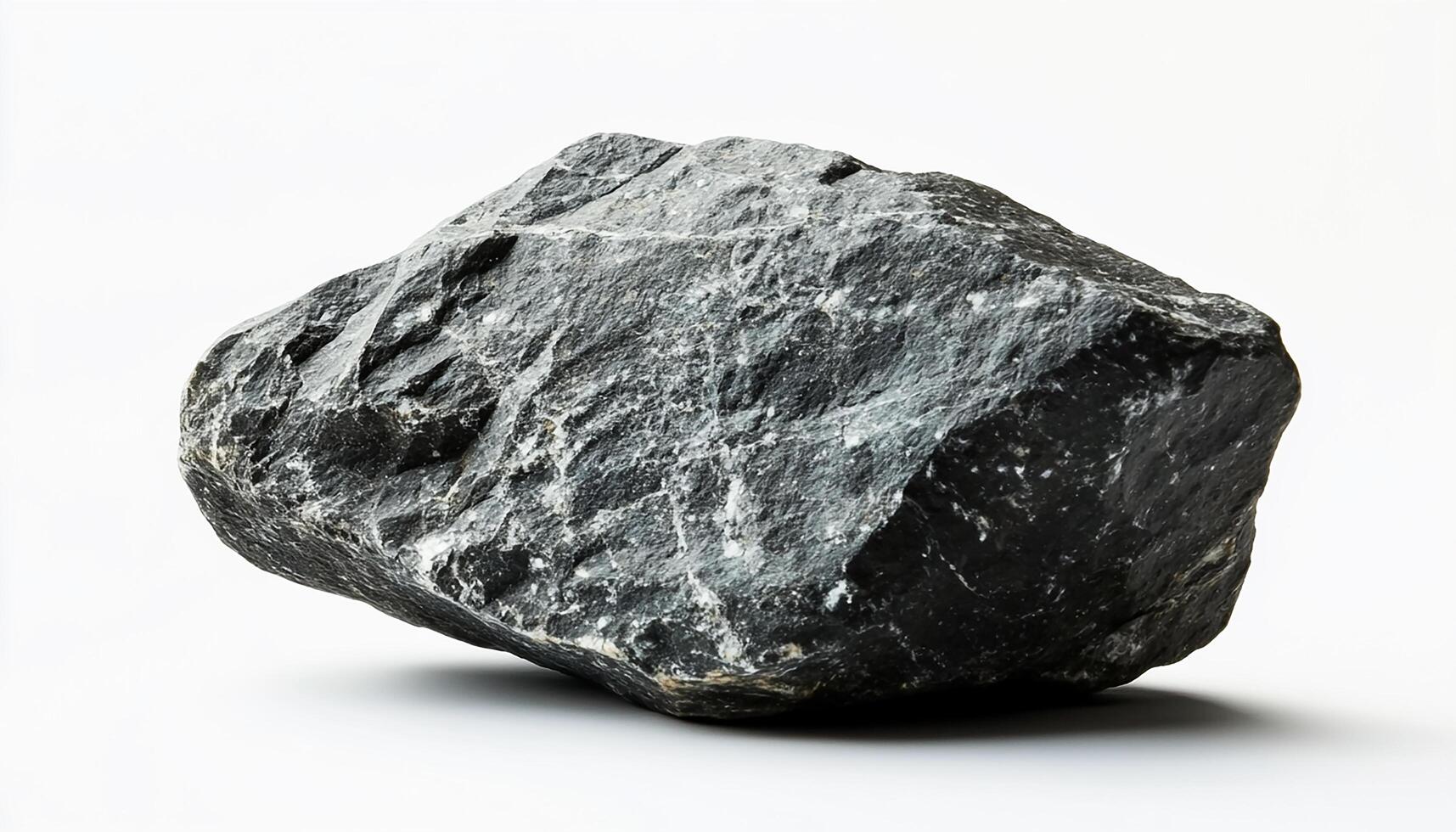 A close up view of a dark gray rock with white streaks against a white background studio shot photo