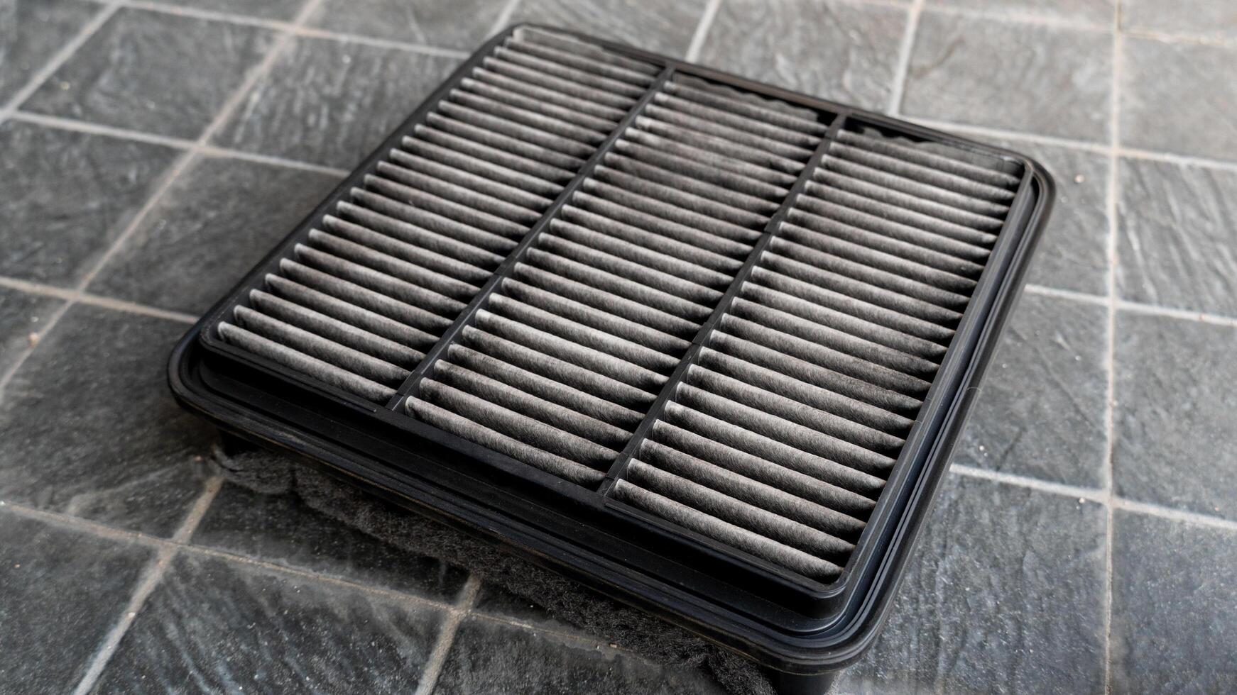 Top view of old engine air filter of car. Cloth panels are covered with black dust. Placed on a black tiled floor. photo
