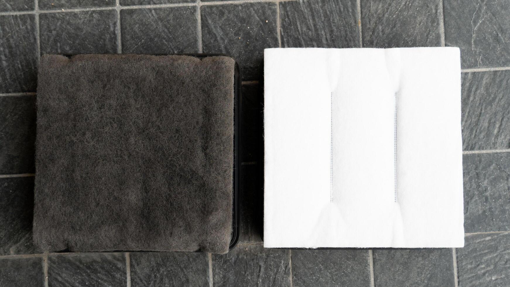 Backside of old and new filters. Comparison between new and old is different. Placed on a black tiled floor. photo