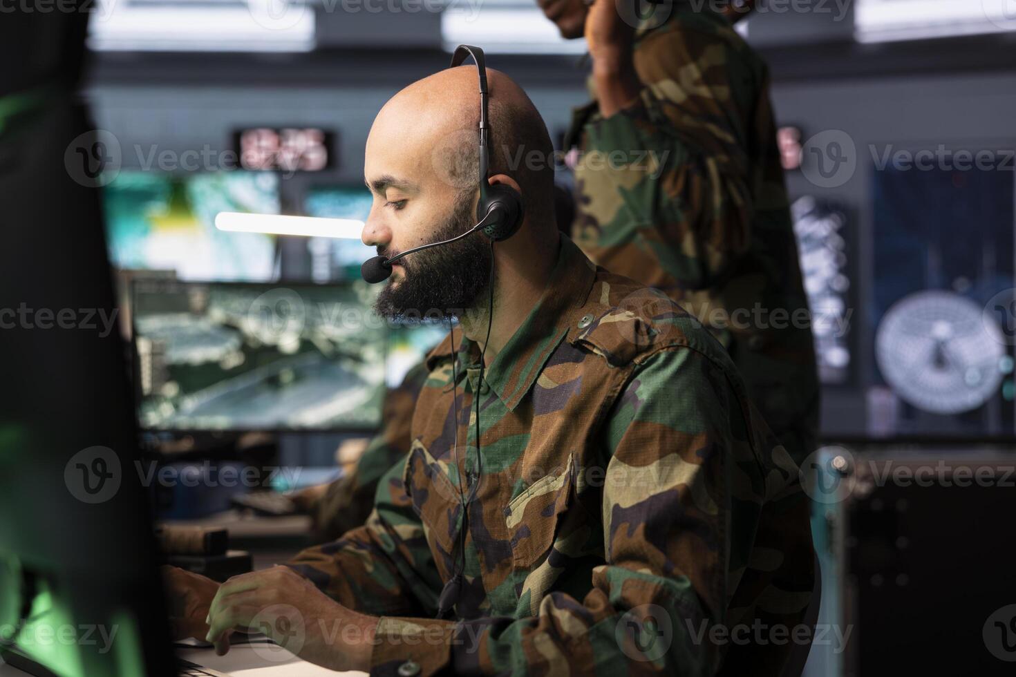 Army dispatcher looking at surveillance transmission on monitors, relaying data to troops using headphones microphone. Military operative transmitting reconnaissance info photo