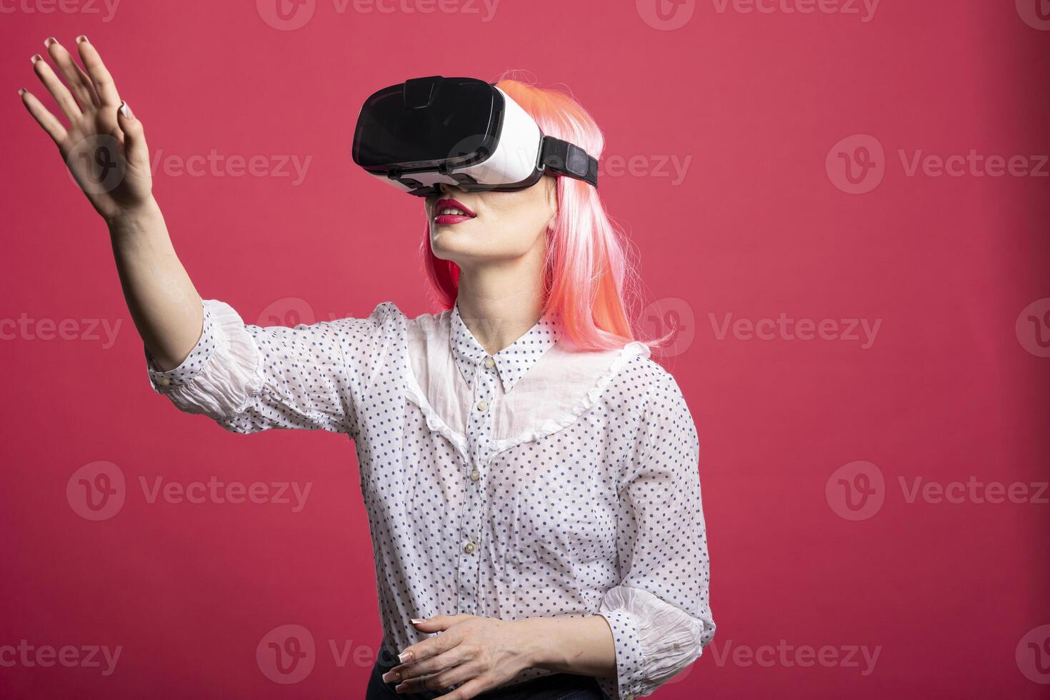 Caucasian female model using VR headset reaching forward with her hand, engaging with futuristic digital world. Young lady in virtual reality gear, immersed in advanced 3D simulation. photo