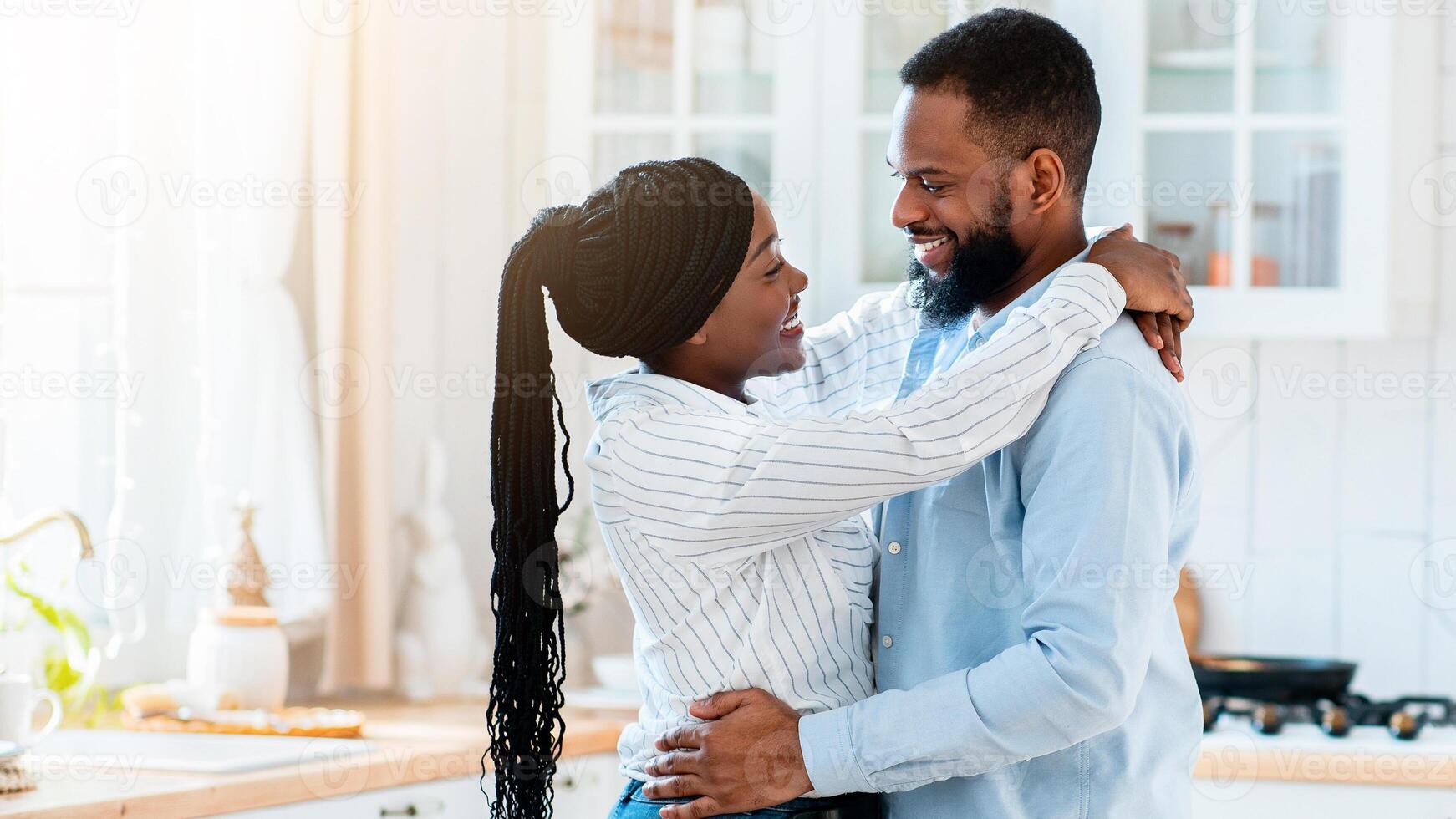 Portrait Of Young Happy Black Man And Woman Ebracing In Kitchen While Having Date At Home, Romantic African American Couple Dancing And Smiling To Each Other, Enjoying Time Together, Side View photo