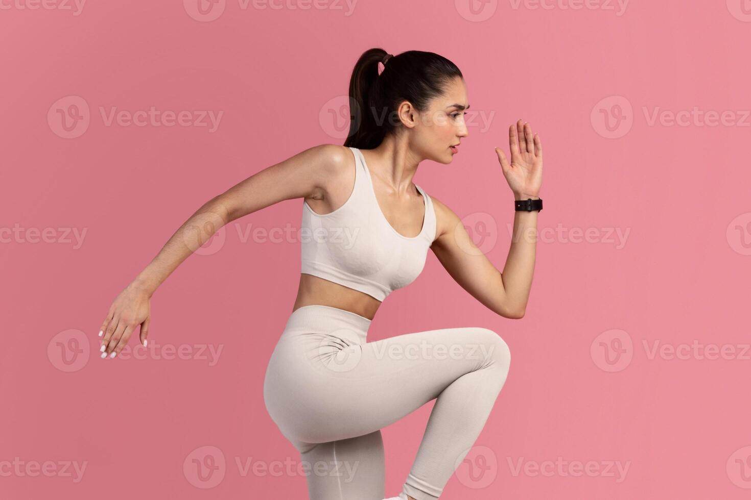 Fitness And Sport Concept. Full Length Portrait Of Confident Fit Young Woman Wearing Activity Tracker Running, Lifting Leg Up, Exercising Isolated On Pink Background, Studio Shot. Energy And Workout photo