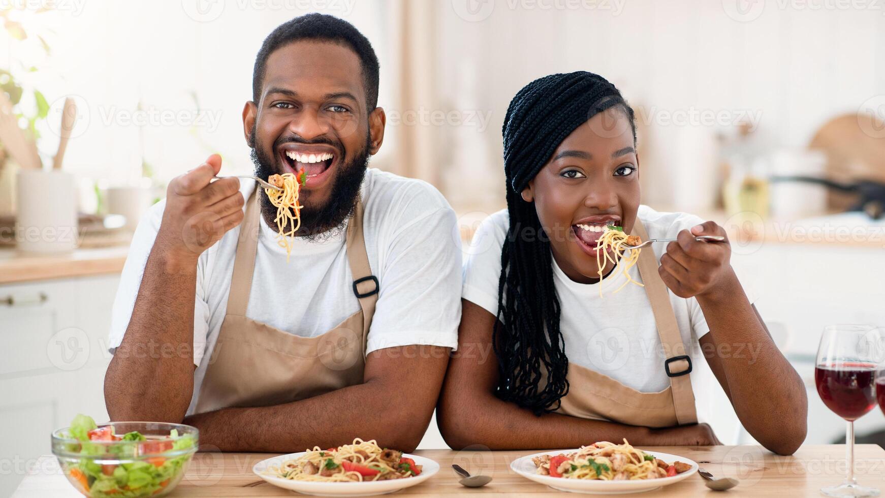 Cheerful Black Spouses Sitting At Table Eating Tasty Lunch In Kitchen, Happy African American Couple Having Spaghetti And Vegetable Salad, Enjoying Delicious Food While Spending Time At Home, Closeup photo