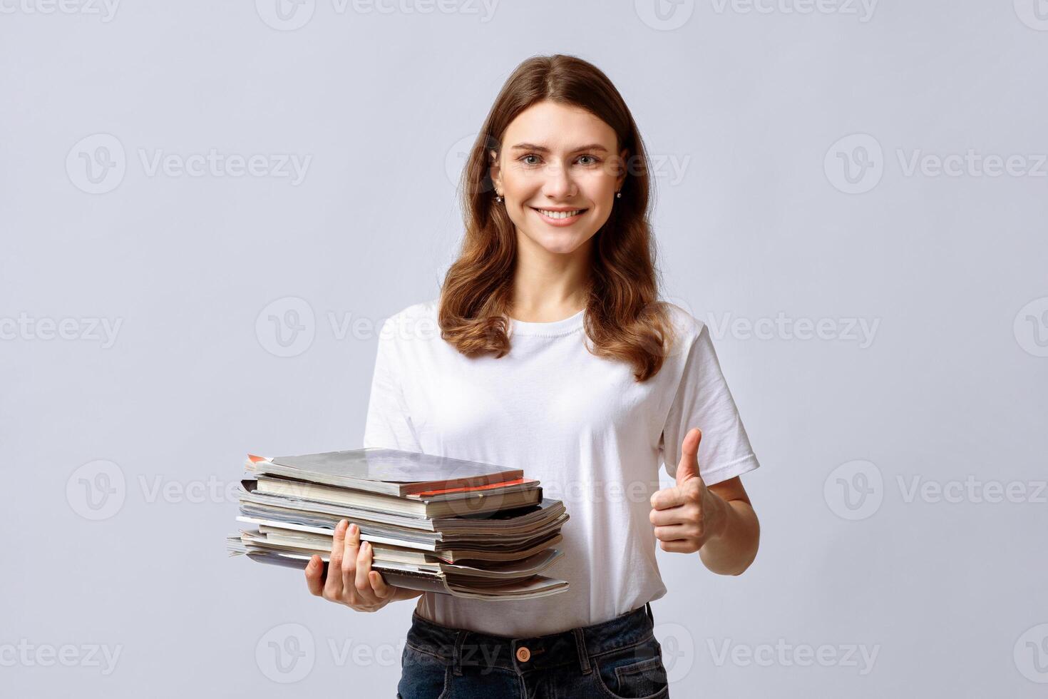 A woman showcases her commitment to recycling by holding a stack of magazines and giving a thumbs up. Her positive attitude highlights the importance of eco-friendly habits in daily life. photo
