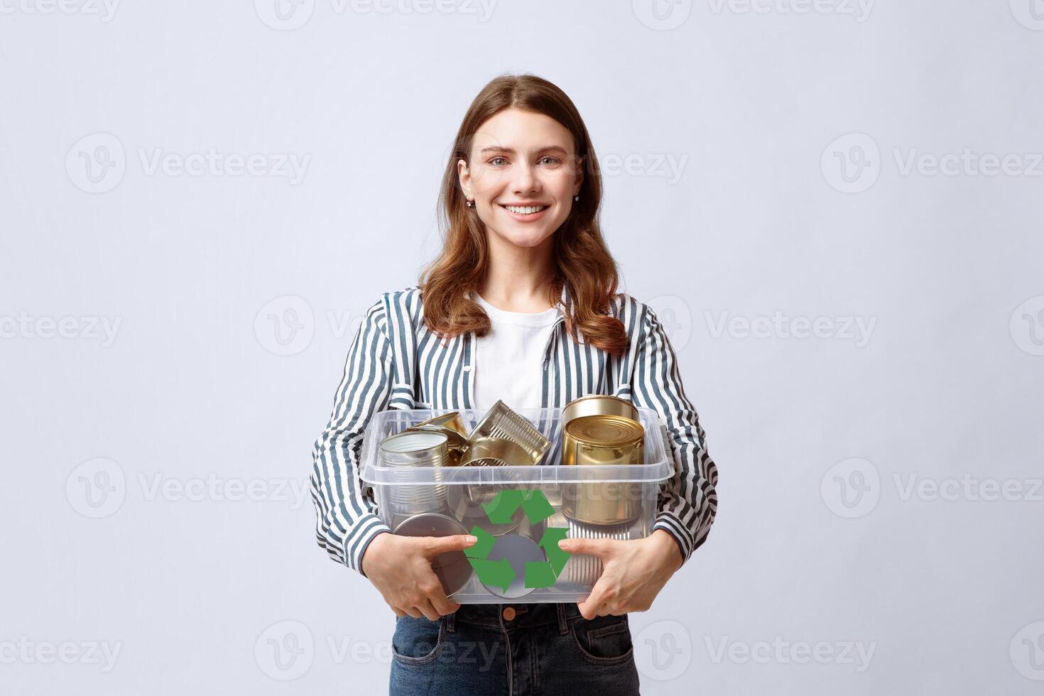 Waste Recycle. Smiling Young Woman Carrying Container Filled With Tin Cans, Millennial Eco Volunteer Lady Enjoying Garbage Recycling, Standing Over Light Gray Background In Studio, Free Space photo
