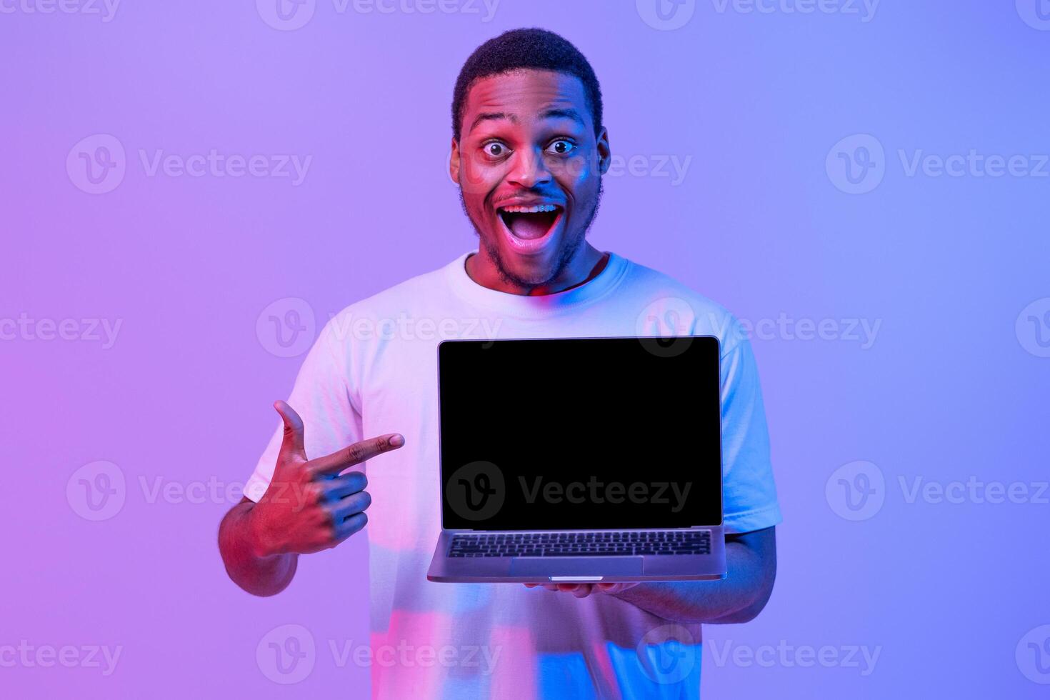 Check This. Overjoyed Black Guy Pointing At Laptop Computer With Blank Screen, Demonstrating Free Copy Place For Your Website Design, Standing In Neon Purple Lighting, Mockup Image photo