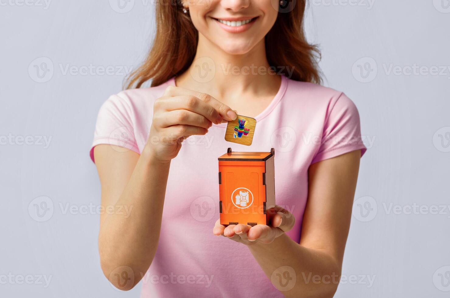 Conceptual Image For Waste Sorting With Young Woman Putting Card With Plastic Trash Icon Into Small Wooden Toy Garbage Bin, Unrecognizable Lady Standing Over Light Background In Studio, Closeup photo