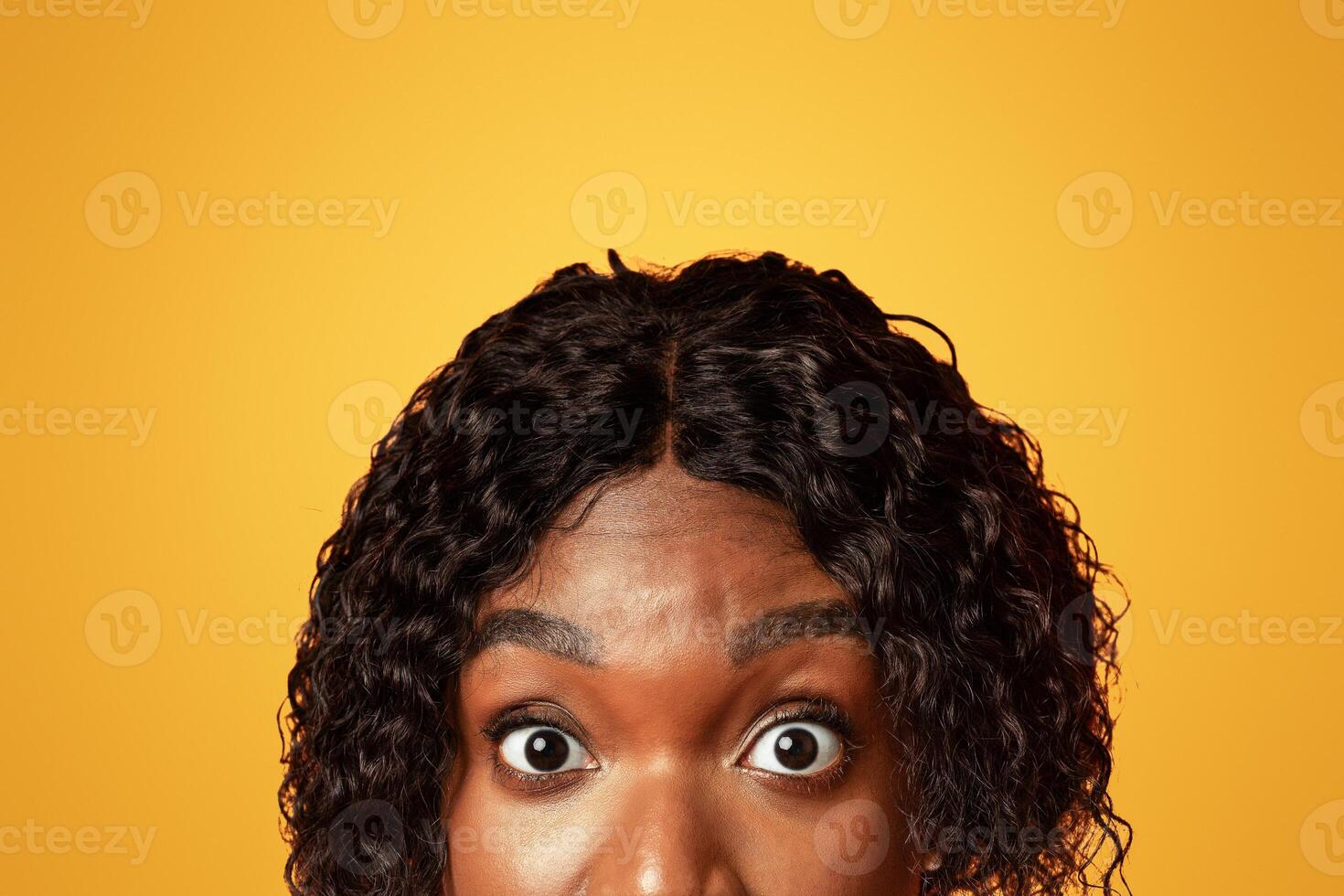 Closeup of millennial black woman surprised eyes, orange studio, background. Amazed african american young lady staring at camera. Emotions and looks, human eyes, face expressions concept photo