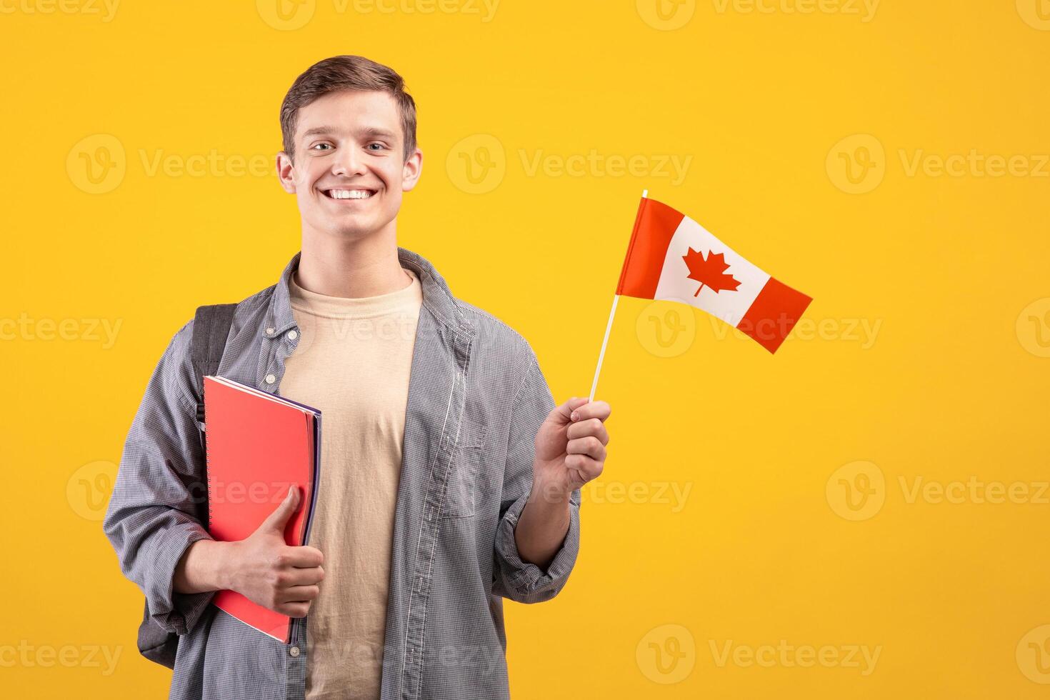 Canada day, patriotism and knowledge sharing. Millennial smiling european guy in casual with backpack, notepads and small flag, isolated on orange background, cut out, copy space, studio shot photo