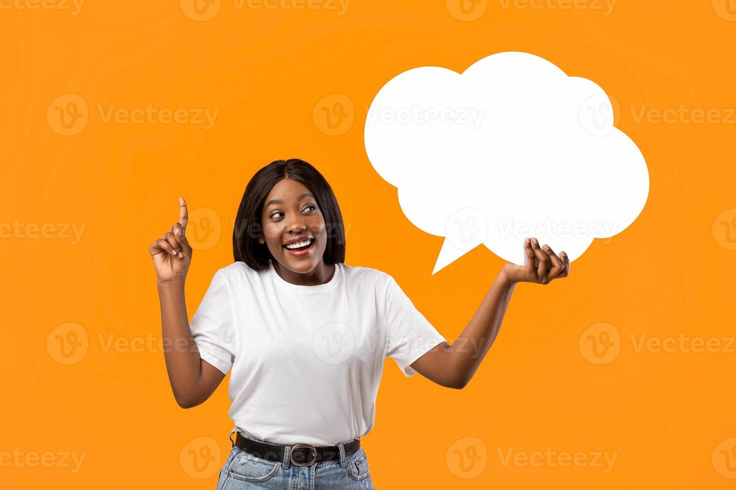 Happy african american young lady holding empty communication bubble and pointing finger up, orange studio background. Black lady in casual with blank clipart, sharing creative ideas photo