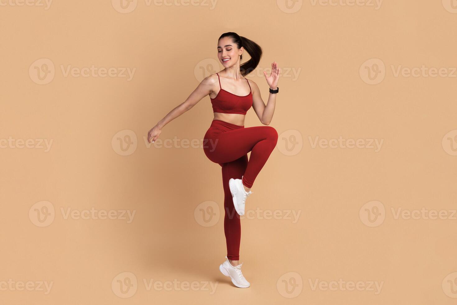 Training Concept. Full Length Portrait Of Smiling Fit Young Lady In Sportswear Jumping And Lifting Leg Up, Exercising Isolated On Pastel Background. Studio Shot, Free Space. Energy And Sports photo