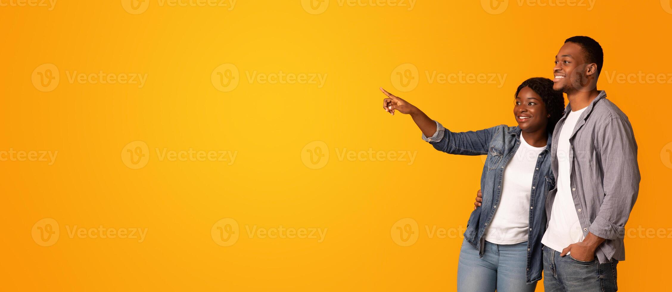 Young Happy Black Couple Pointing With Finger Aside At Copy Space, Excited Young African American Man And Woman Embracing And Looking At Free Place Over Yellow Background, Panorama photo