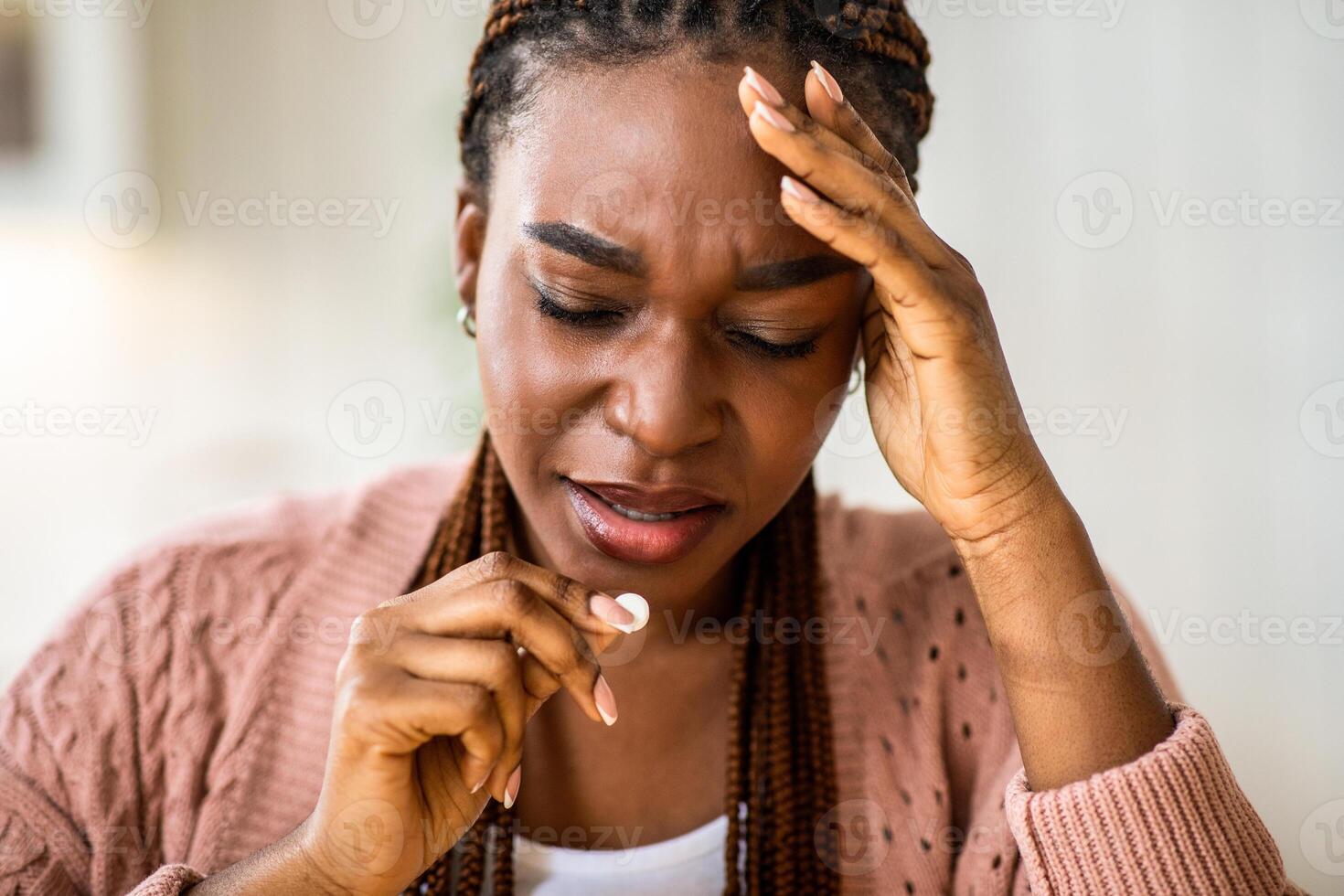 Upset black lady suffering from headache or migraine at home and taking pill, african american woman feeling unwell, holding her head, having acute pain, using painkiller tablet, closeup shot photo