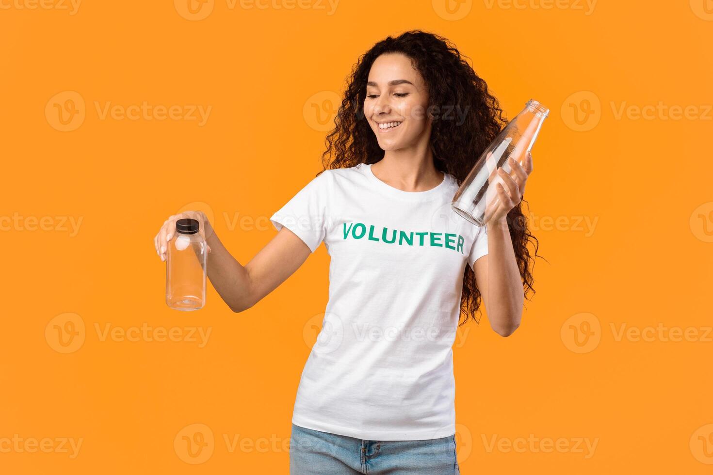 No More Plastic. Female Volunteer Choosing Between Glass And Plastic Bottle Posing Standing In Studio Over Yellow Background. Stop Using Single-Used Bottles, Ecology Concept photo