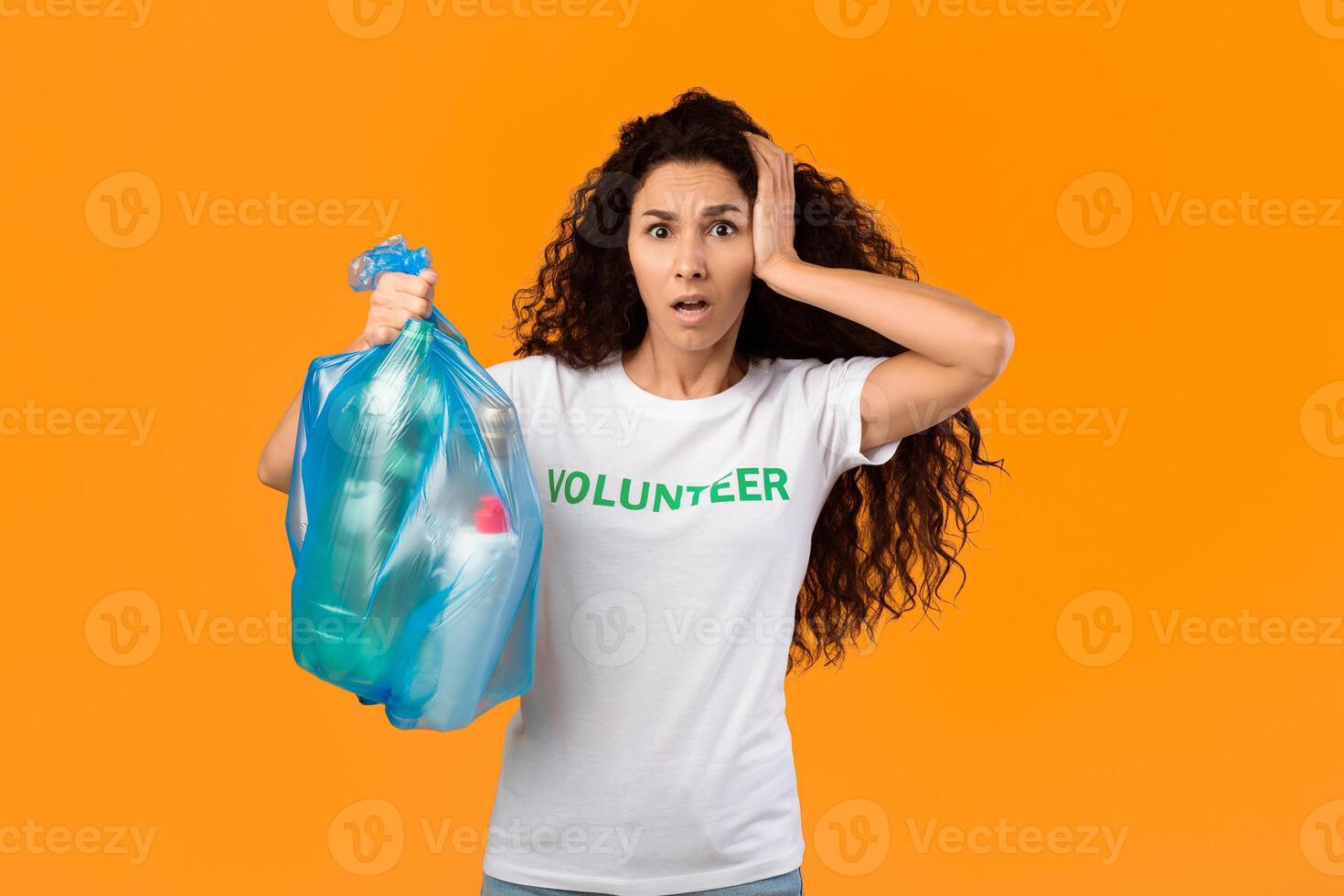 Shocked Volunteer Woman Holding Plastic Garbage Bag With Litter Looking At Camera Standing On Yellow Studio Background. Unsorted Waste And Pollution Problem, Junk Sorting Concept photo