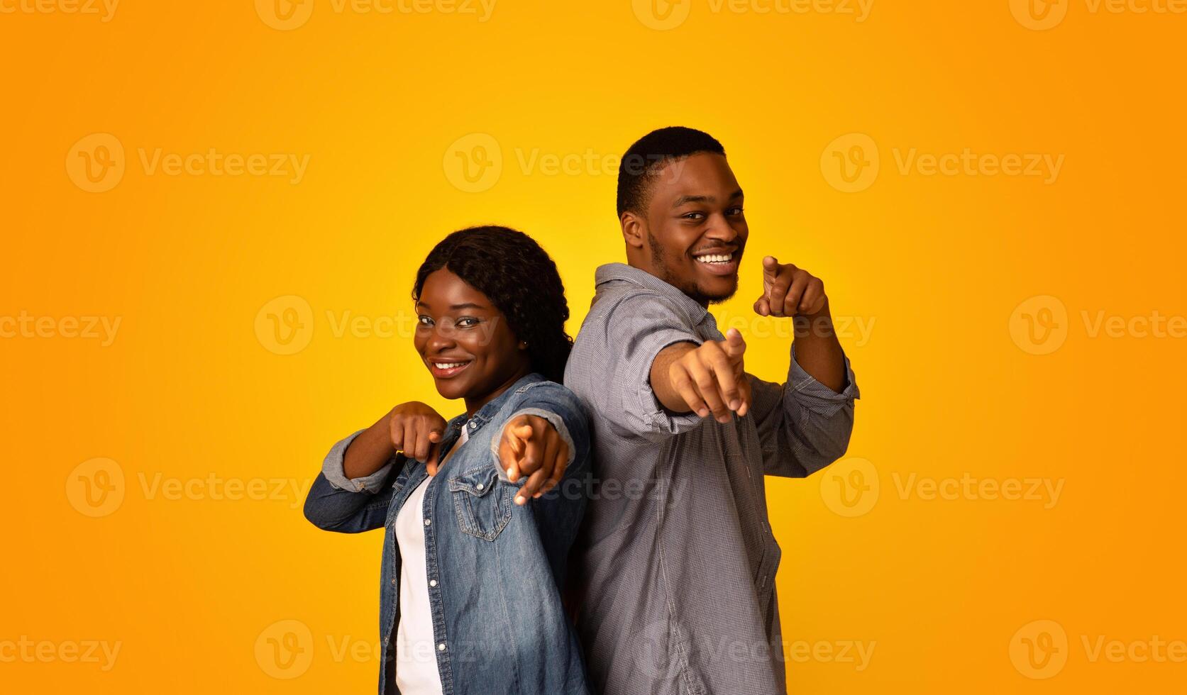 Gotcha. Joyful african man and woman pointing at camera with fingers, cheerful black millennial couple indicating somebody, having fun while standing isolated over yellow background, free space photo