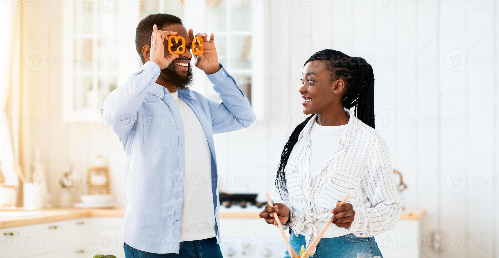 Positive Young Black Spouses Having Fun While Cooking In Kitchen At Home, Cheerful Husband Making Eyeglasses From Bell Pepper Slices, African American Spouses Enjoying Healthy Preparing Food Together photo