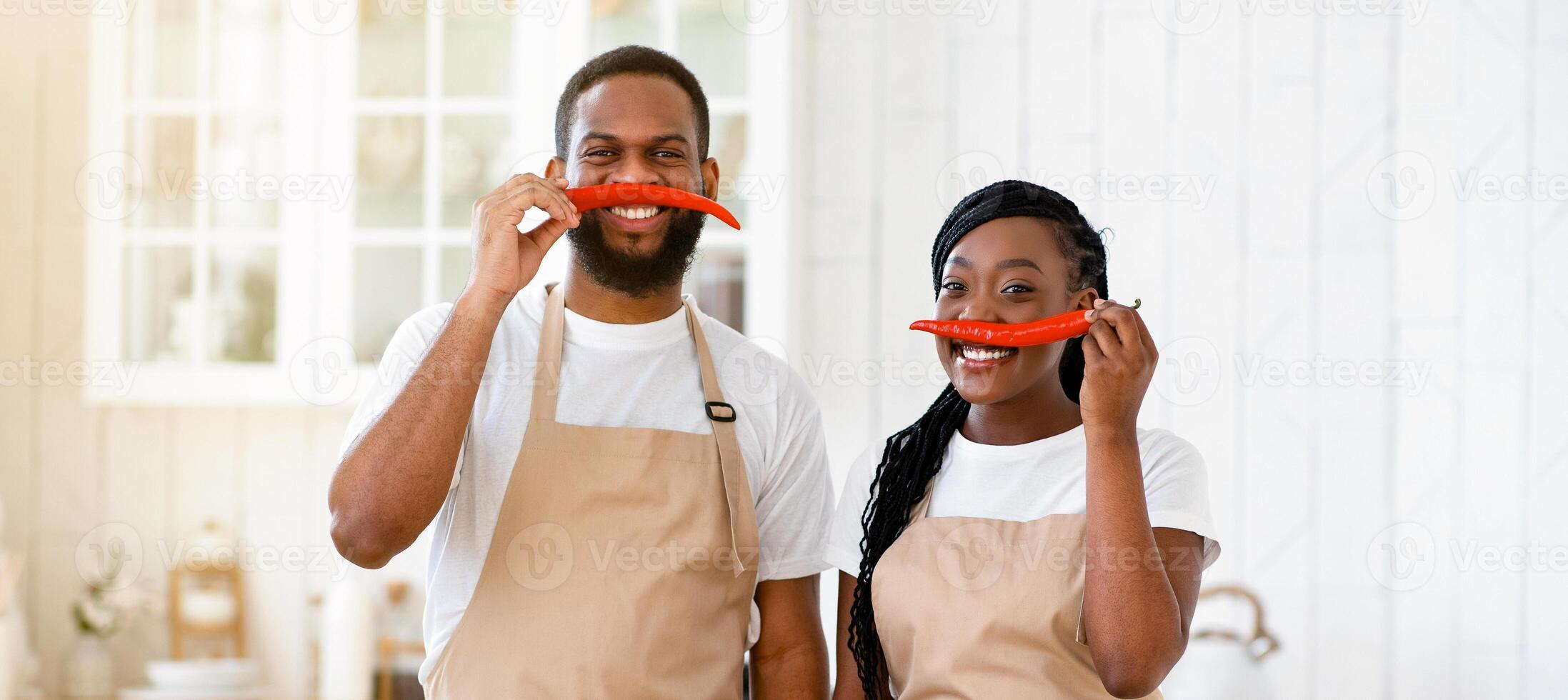 Happy african american couple having fun while cooking in kitchen, keeping pepper as moustache and smiling at camera, funny black young spouses enjoying preparing food together, free space photo