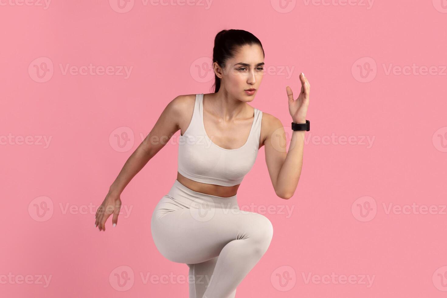 Sport Exercises And Healthy Lifestyle. Full Length Portrait Of Determined Slim Young Lady Running And Sprinting, Wearing Fitness Bracelet, Lifting Leg Up, Exercising Isolated On Pink Studio Background photo