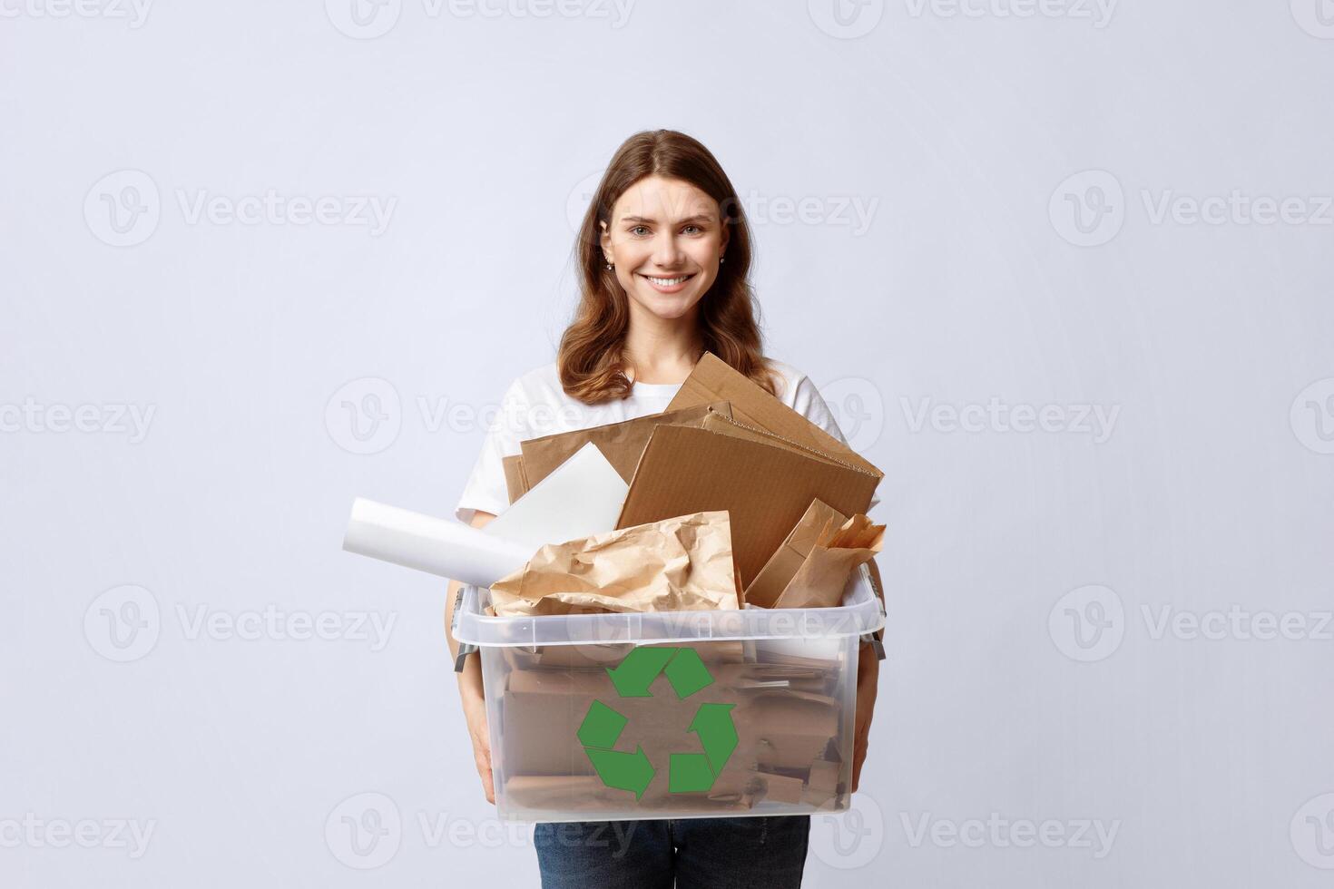 Recycling And Waste Sorting Concept. Smiling Young Woman Holding Plastic Box With Paper Garbage, Standing Over Light Background In Studio, Portrait Of Millennial Eco-Friendly Lady, Copy Space photo