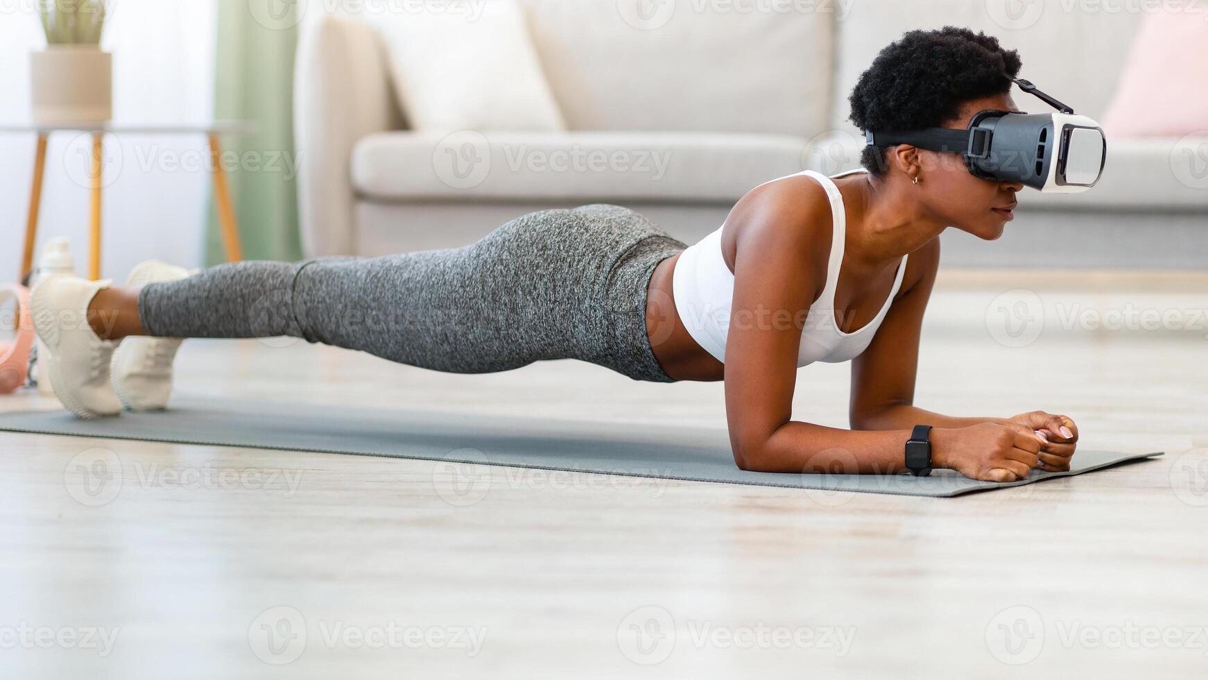 VR Workout. Black Fitness Lady Standing In Plank Wearing VR Headset Exercising During Training In Virtual Gym At Home. Augmented Reality Application For Smart Sport. Side View photo
