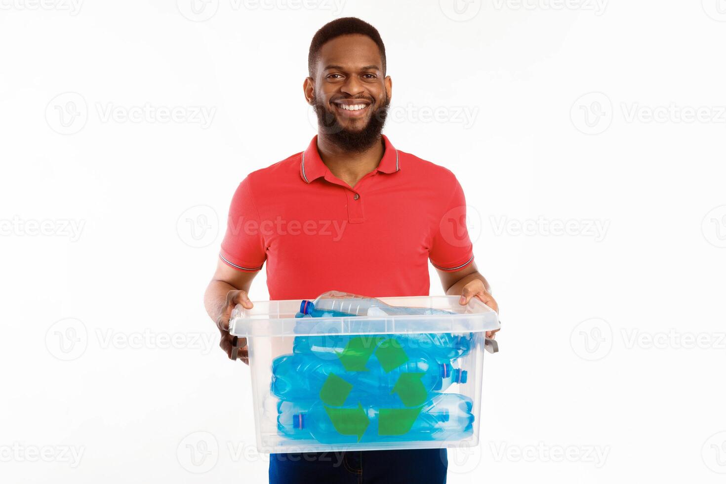 Black Guy Holding Box With Recycle Symbol Full Of Used Plastic Bottles Sorting His Waste For Disposal Standing On White Studio Background, Smiling To Camera. Junk Sorting And Recycling Concept photo