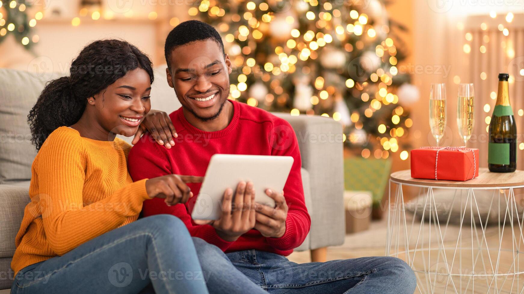 Home cozy in New Year and Christmas and call to friends or family. Happy millennial african american lovers guy and lady talking on digital tablet in living room interior with tree with garlands photo
