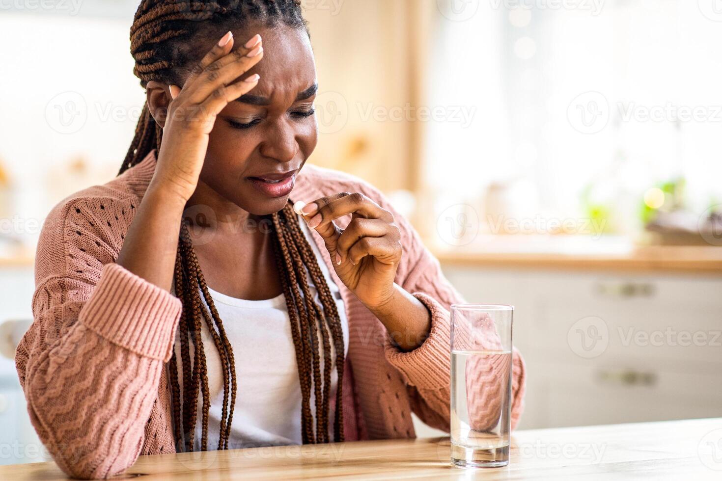 Stressed Black Lady Taking Painkiller Pill While Sitting At Table In Kitchen, Upset African American Woman Suffering From Headache Or Migraine, Drinking Medicine To Reduce Acute Pain, Free Space photo
