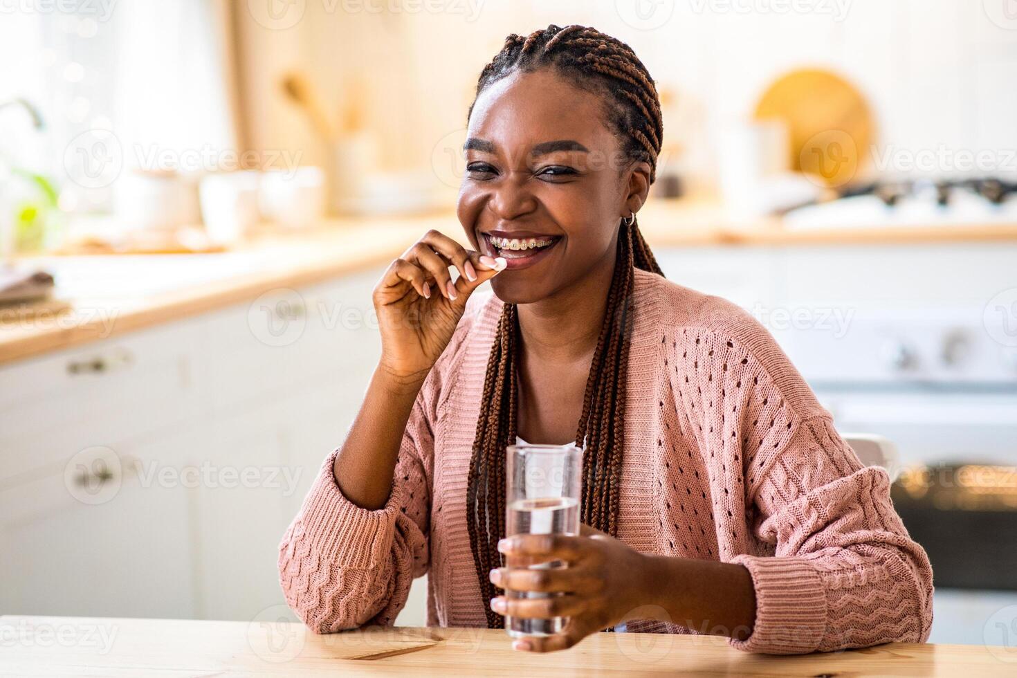 Cheerful Young African American Lady Taking Beauty Supplement Pill In Kitchen, Happy Black Millennial Woman Sitting At Tablet, Eating Multivitamin Tablet And Drinking Water At Home, Free Space photo