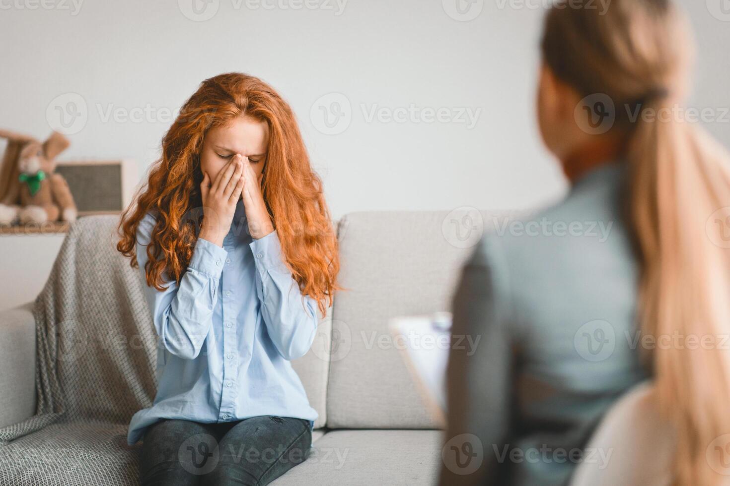 Psychological Consultation. Child psychologist working with teenager in office or at home, worried sad girl crying, covering her face, talking about family problems, feeling stress, sitting on couch photo