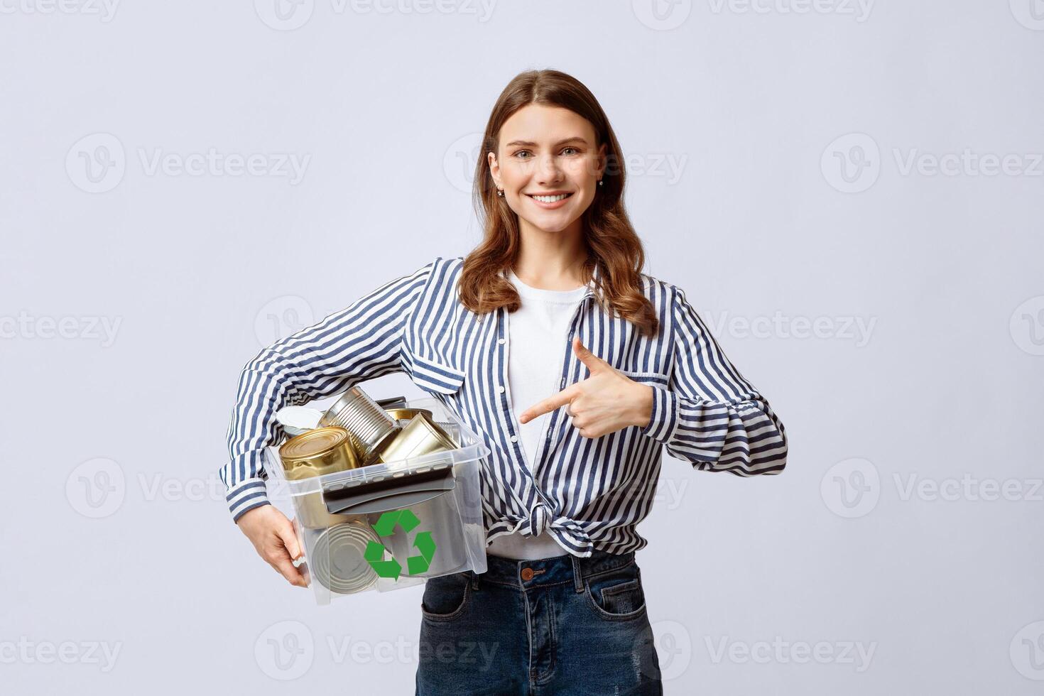Metal Recycle. Positive Millennial Lady Holding And Pointing At Plastic Container With Aluminum Cans, Young Eco-Activist Woman Enjoying Waste Sorting System, Standing On Light Background, Free Space photo