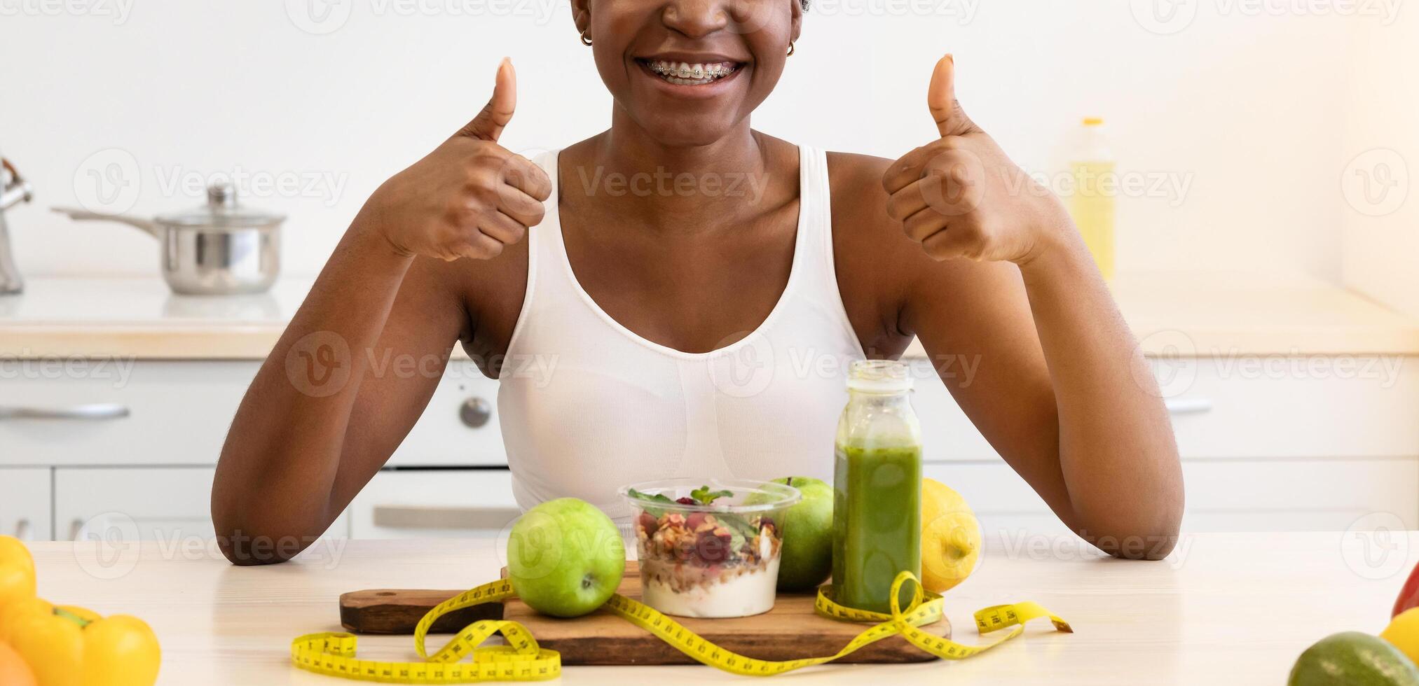 I Like Healthy Eating. Black Fit Lady Gesturing Thumbs Up Sitting Near Table With Natural Food And Smoothie Having Dinner For Slimming In Modern Kitchen At Home. Weight Loss Diet, Health And Nutrition photo