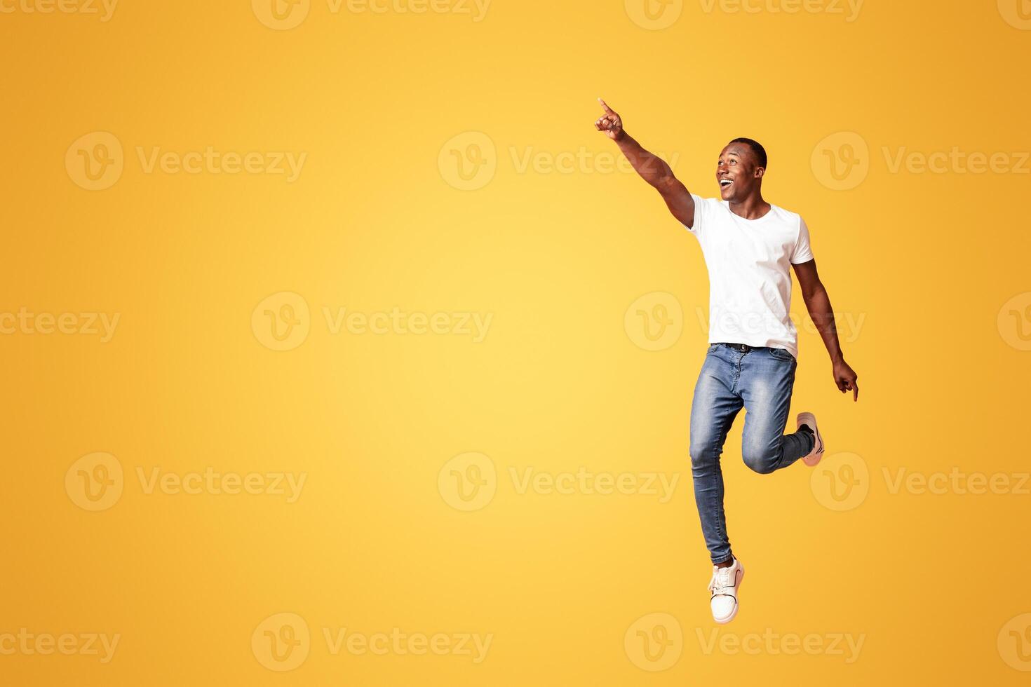 Emotional black man jumping and pointing at copy space for advertising or announcement on orange background, studio full length shot. Cheerful african american guy showing great advertisement photo