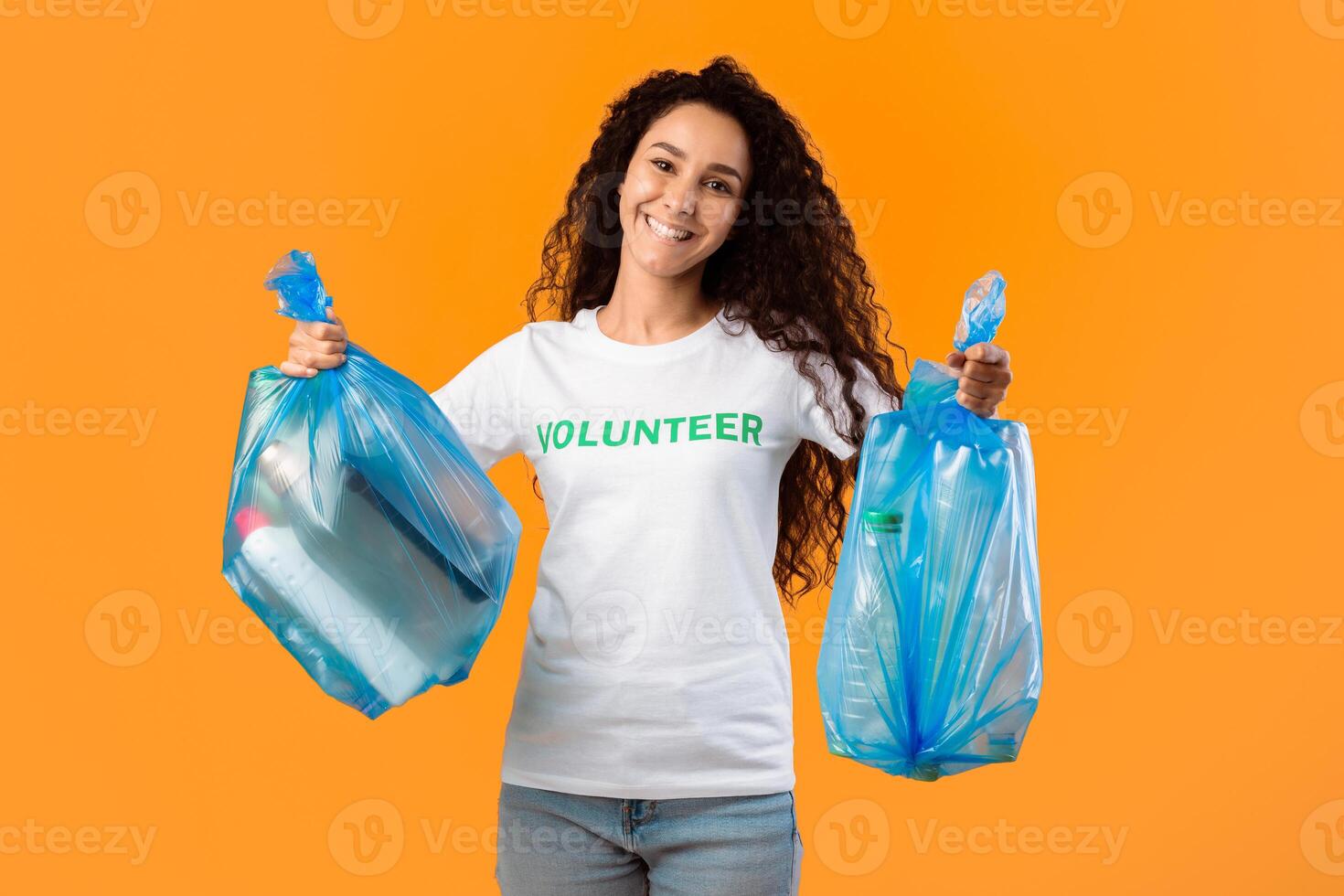 Sort Your Waste. Volunteer Lady Holding Blue Plastic Garbage Bags Posing Smiling To Camera Standing In Studio Over Yellow Background. Litter And Trash Sorting, Clean Environment Concept photo