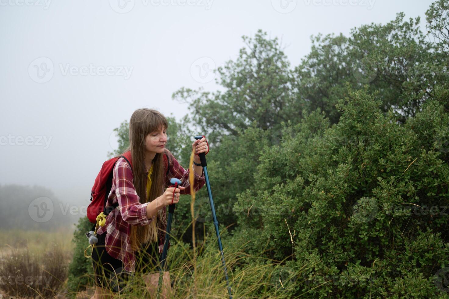 Young Woman Hiking Through Foggy Forest with Trekking Poles photo