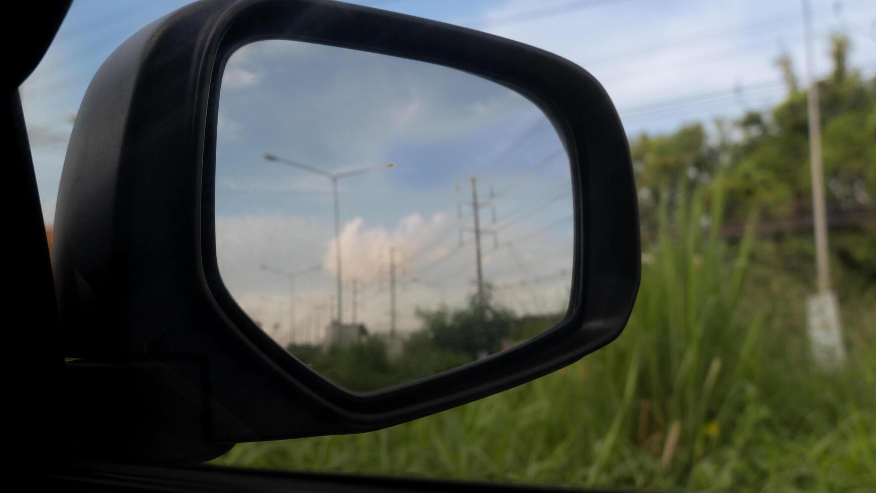 Inside view of mirrors wing. Beside car with green grass. Inside mirror wing with top of grass under the sky. photo