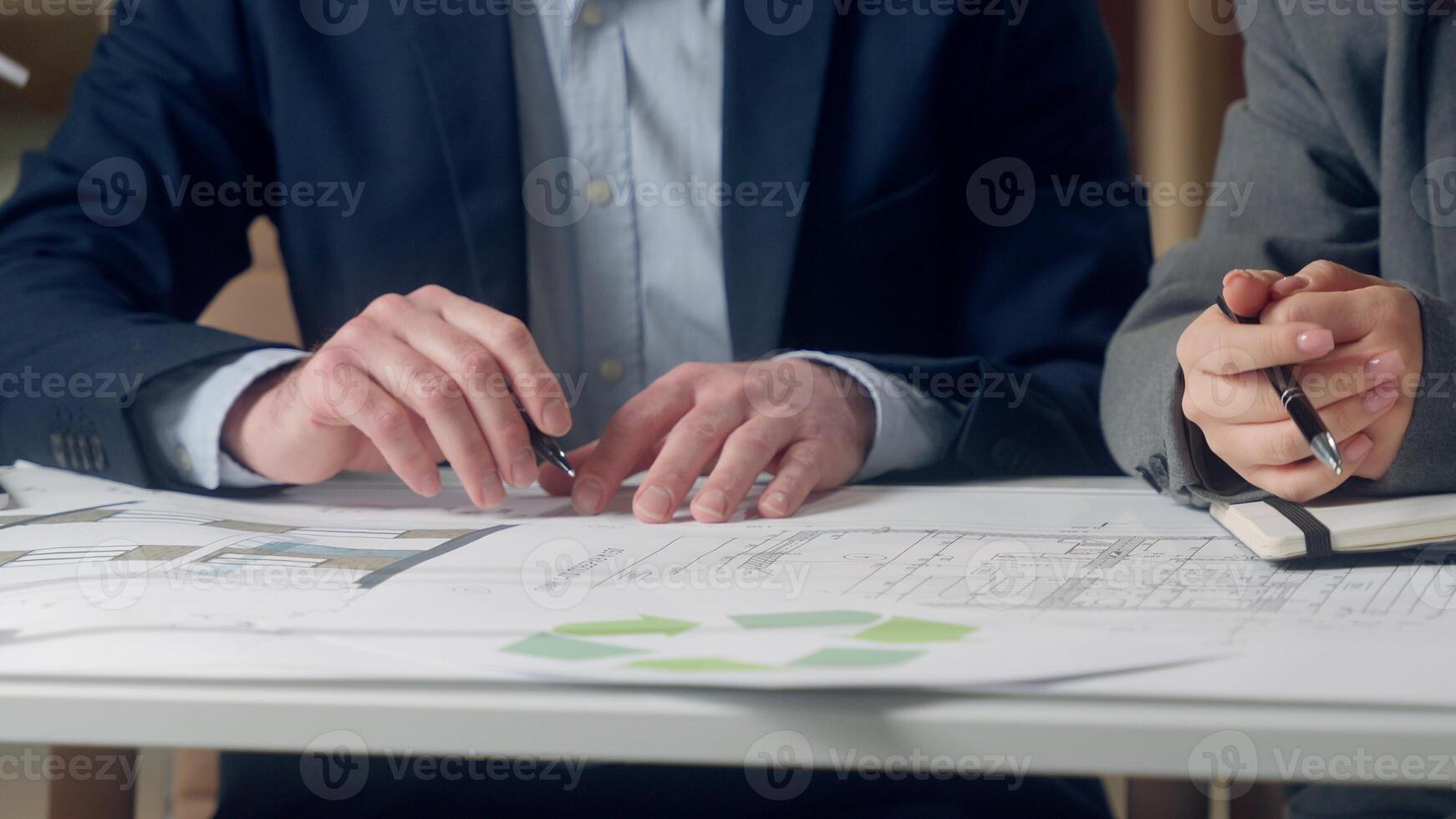Korean woman specialist Caucasian man pointing pen explain blueprint windmill model sustainable development energy multinational teamwork talk engineering discussion eco electricity innovation office photo