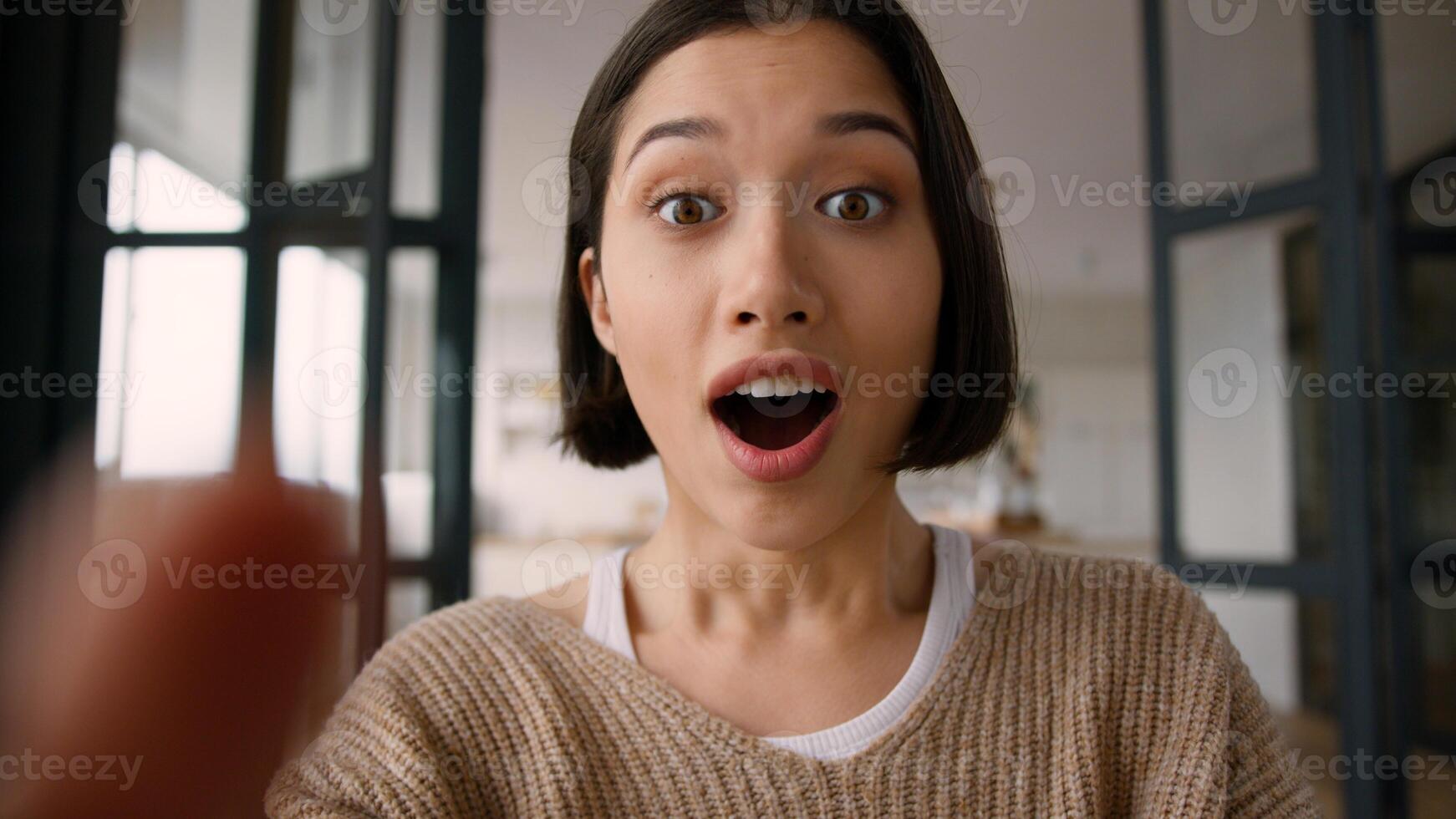Point of view POV webcam mobile phone happy amazed excited girl Hispanic latin woman astonish wonder shock emotions read good news online app win typing message fingers touch screen display smartphone photo