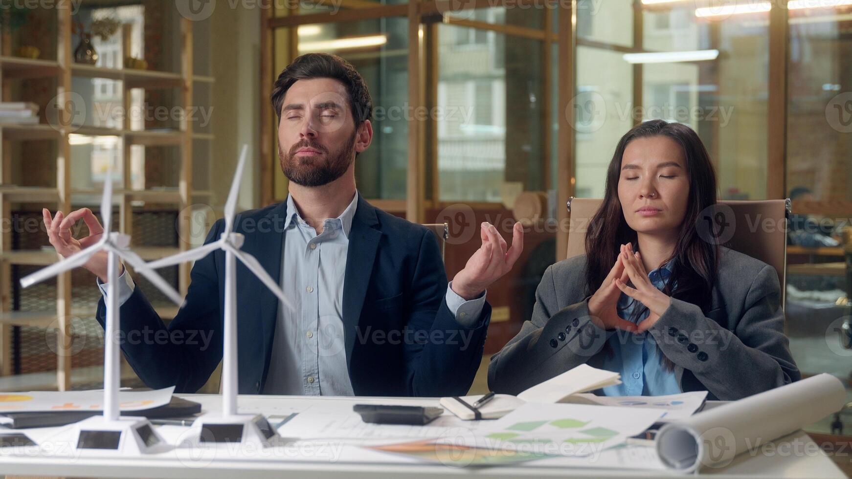 Multiethnic relaxed business team meditating wind turbine startup windmill models eco engineers Korean woman Caucasian man stress relief sustainable energy green focus harmony innovation peaceful rest photo