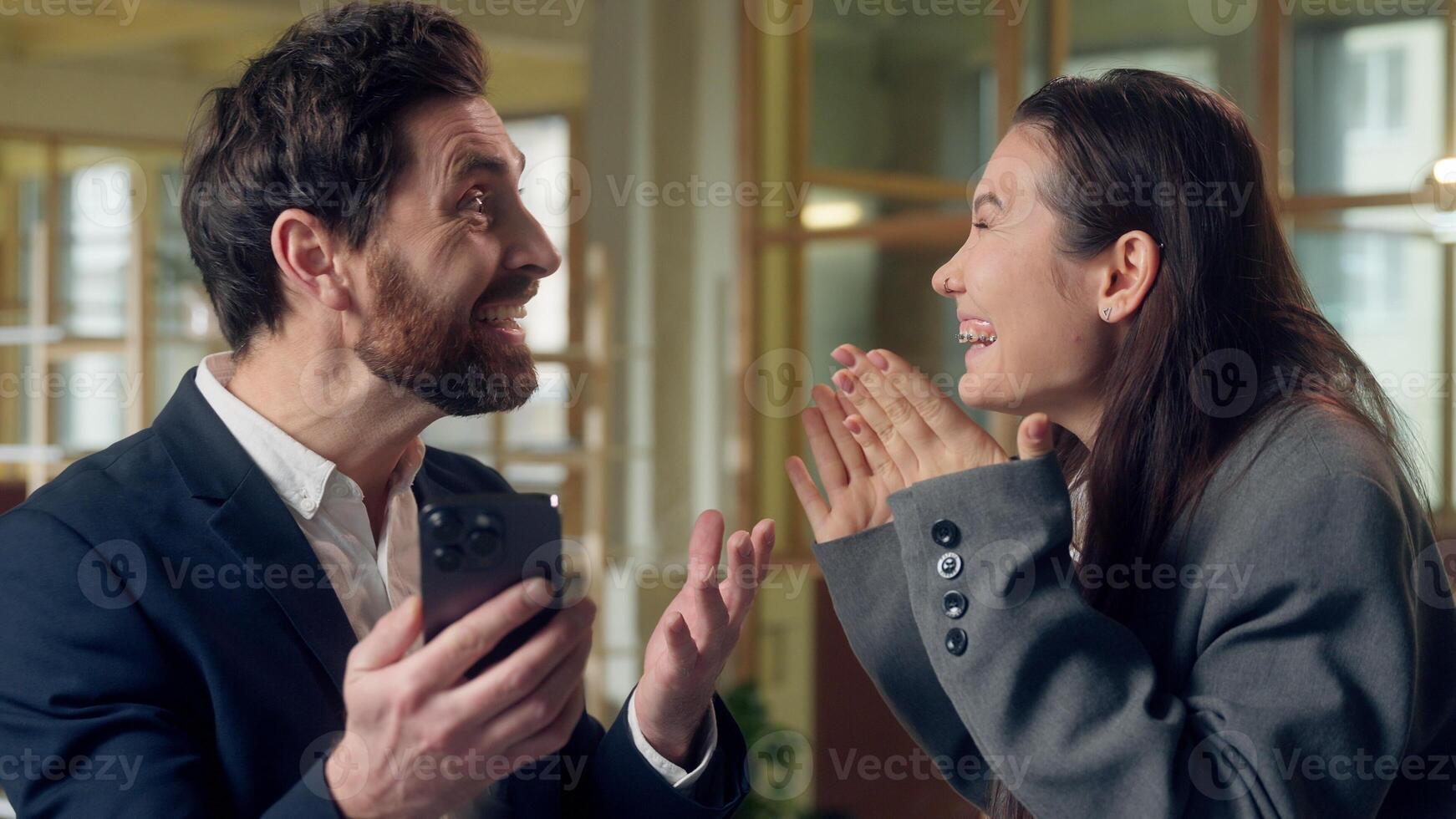 Excited shocked Caucasian Korean business man woman using mobile phone success at office winning deal offer businessman businesswoman partners coworkers look smartphone cheering online victory triumph photo